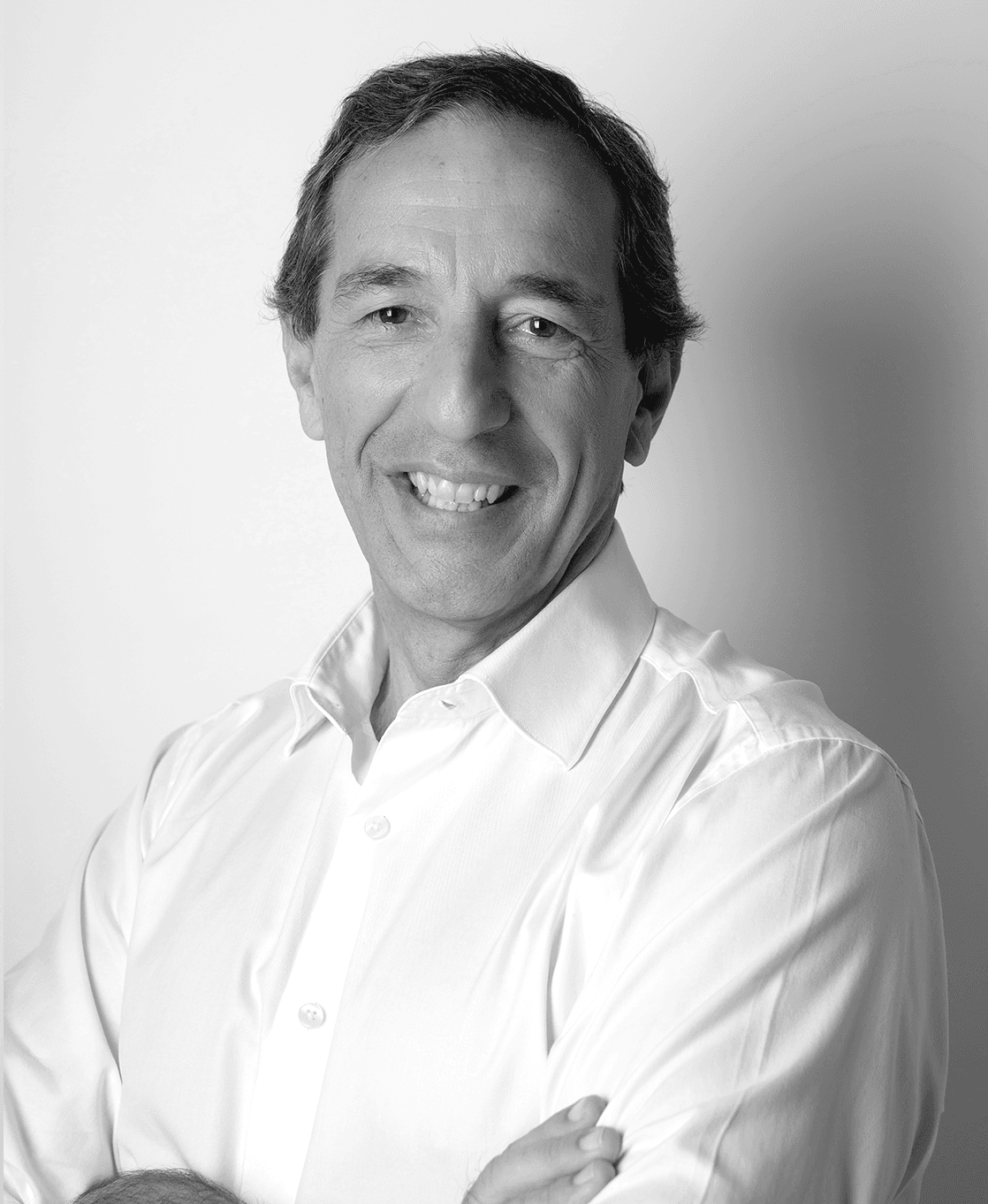 Portrait of CEO Jorge Alcobia in a white shirt, standing in front of a white wall, smiling at the camera