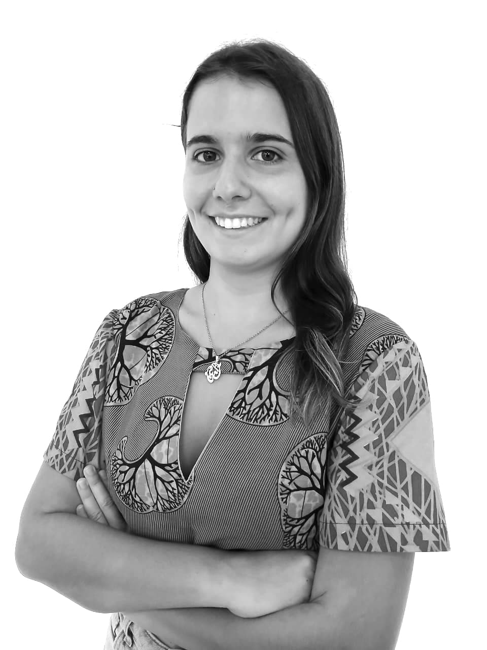 Rita Vieira stands in front of a white wall, wearing a blouse, smiling at the camera