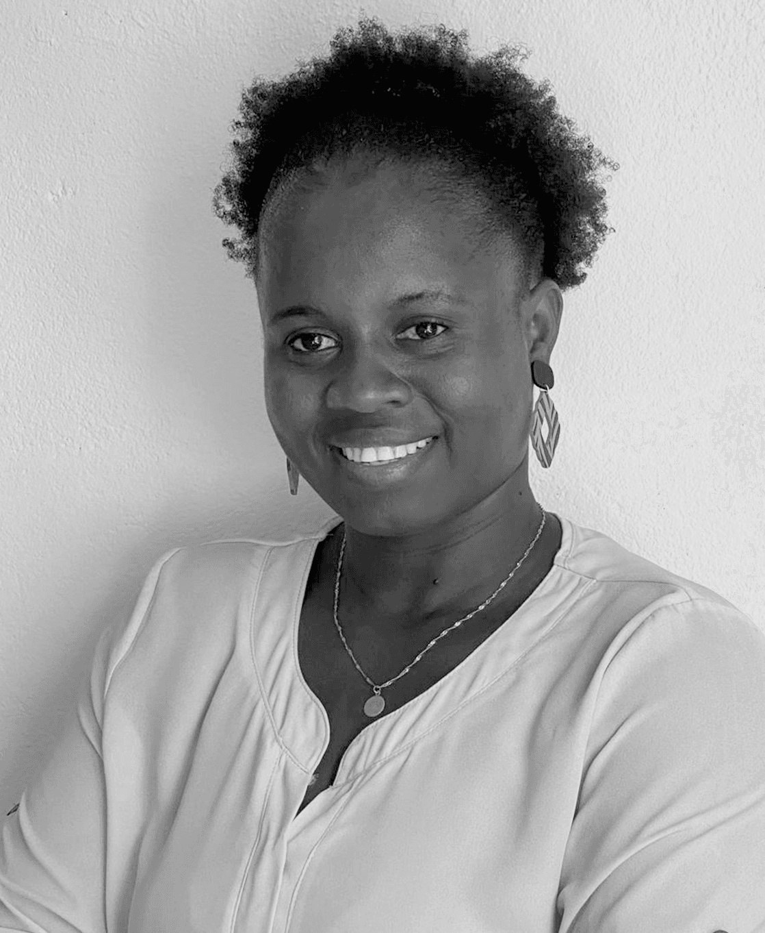 Portrait of Emelinda Mendes in a white blouse, standing in front of a white wall, smiling at the camera