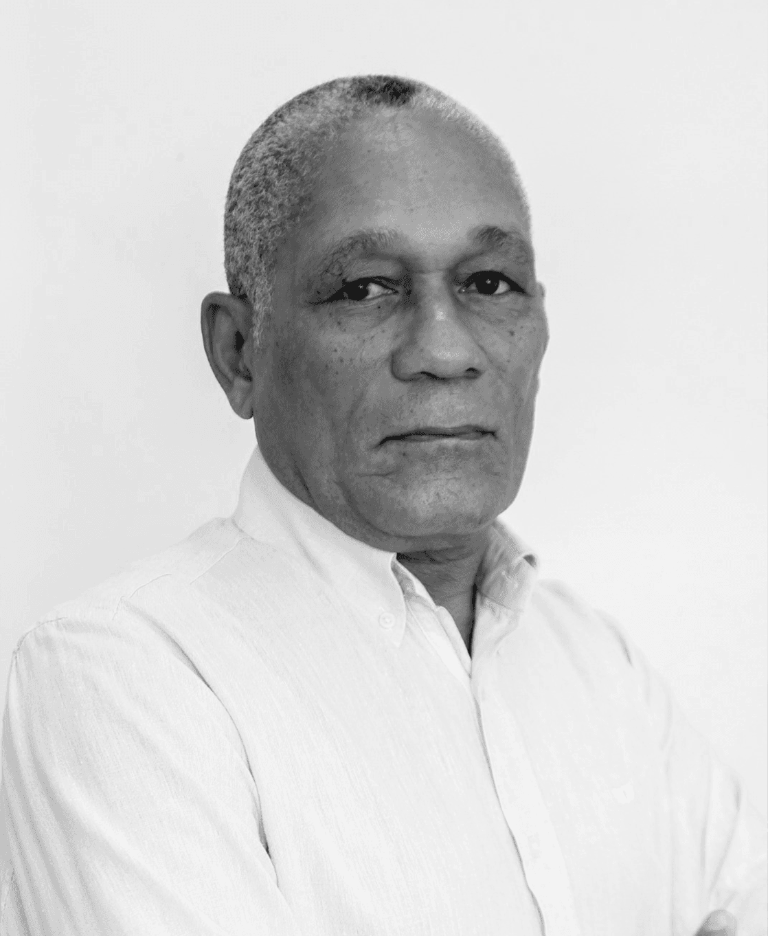 Horacio Dias stands in front of a white background, wearing a white shirt and looking at the camera