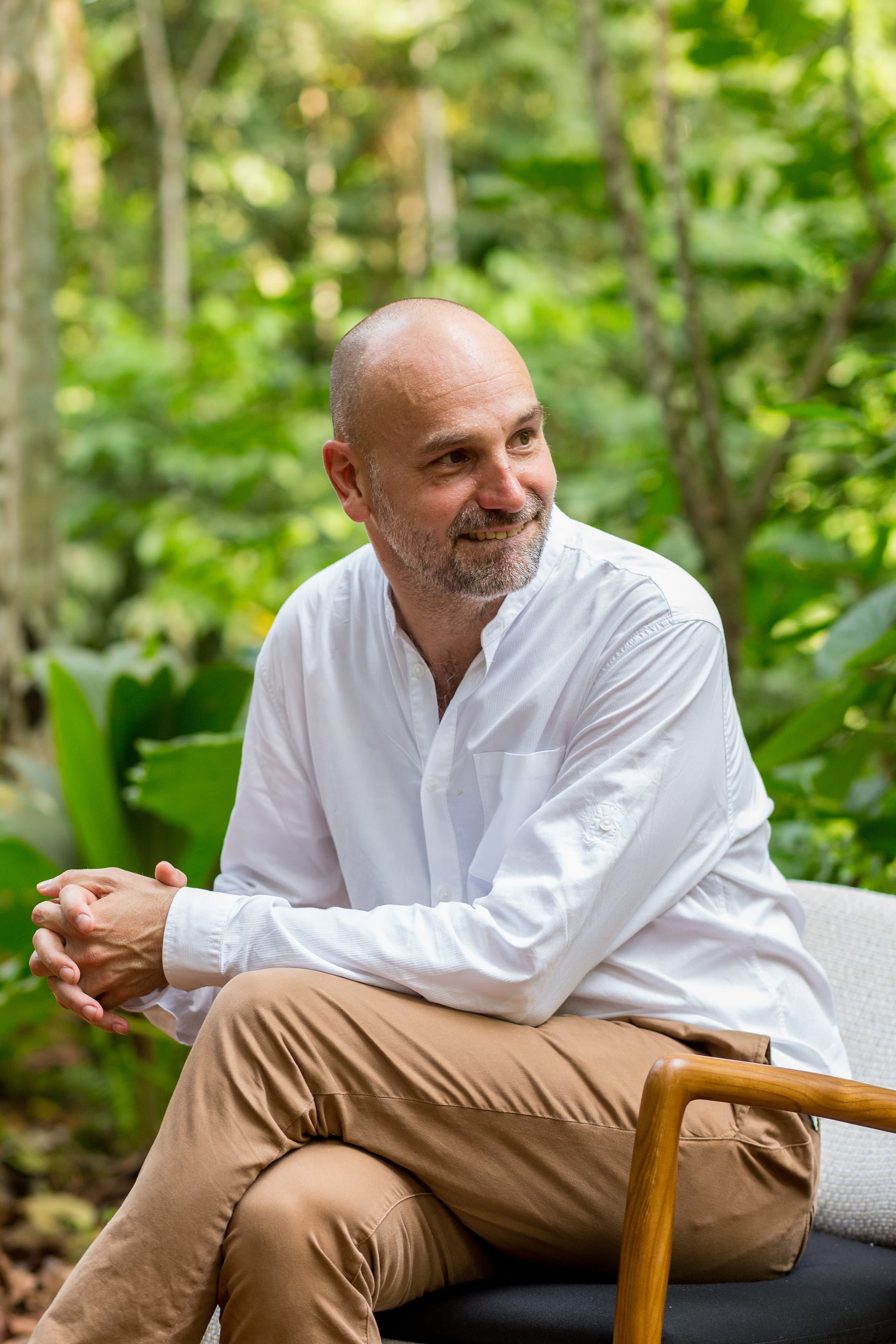 Mark Shuttleworth in a white shirt sits in front of dense green vegetation on Príncipe Island