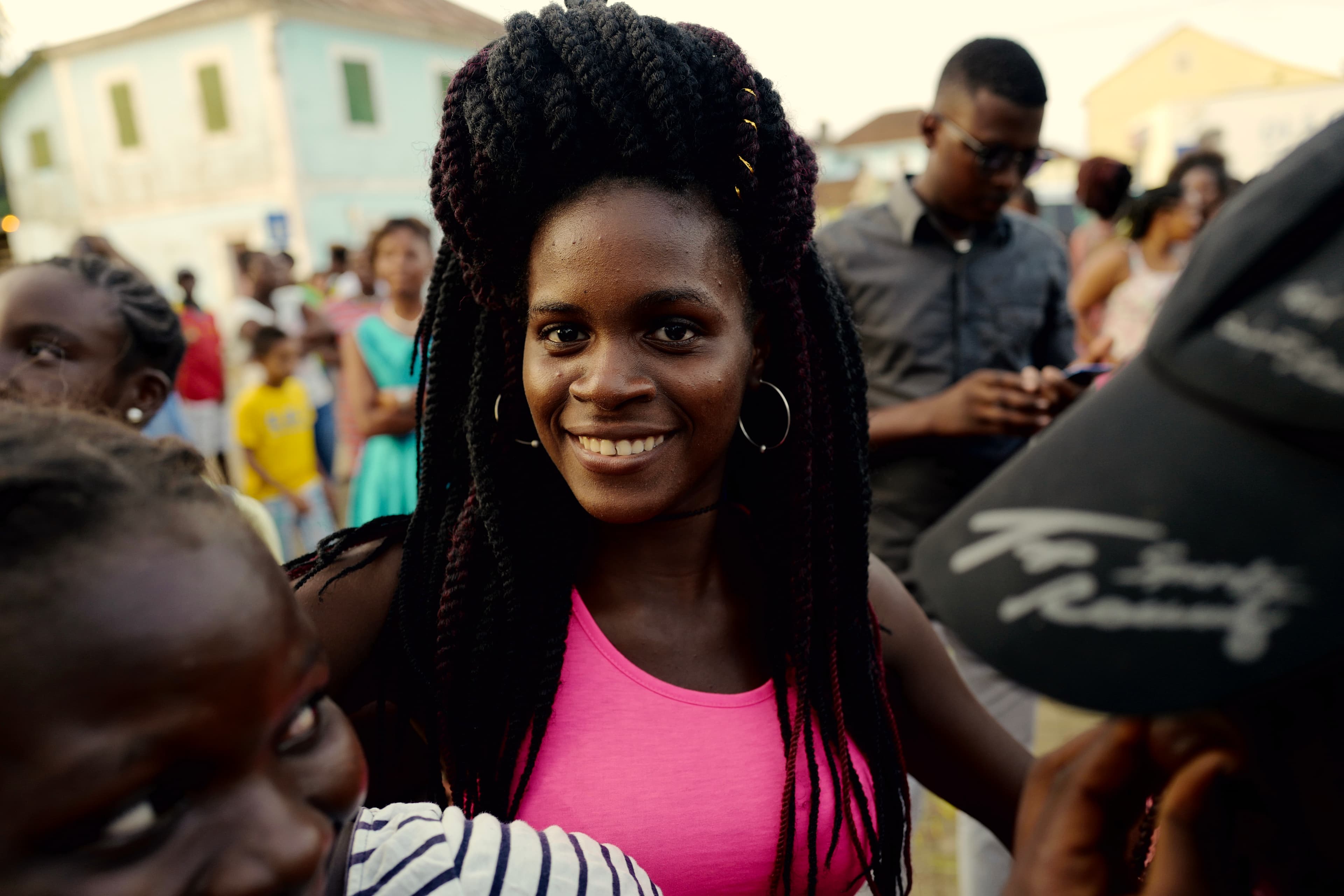 Beautiful young lady in a pink shirt and round earrings stands in a crowd, smiling at the camera