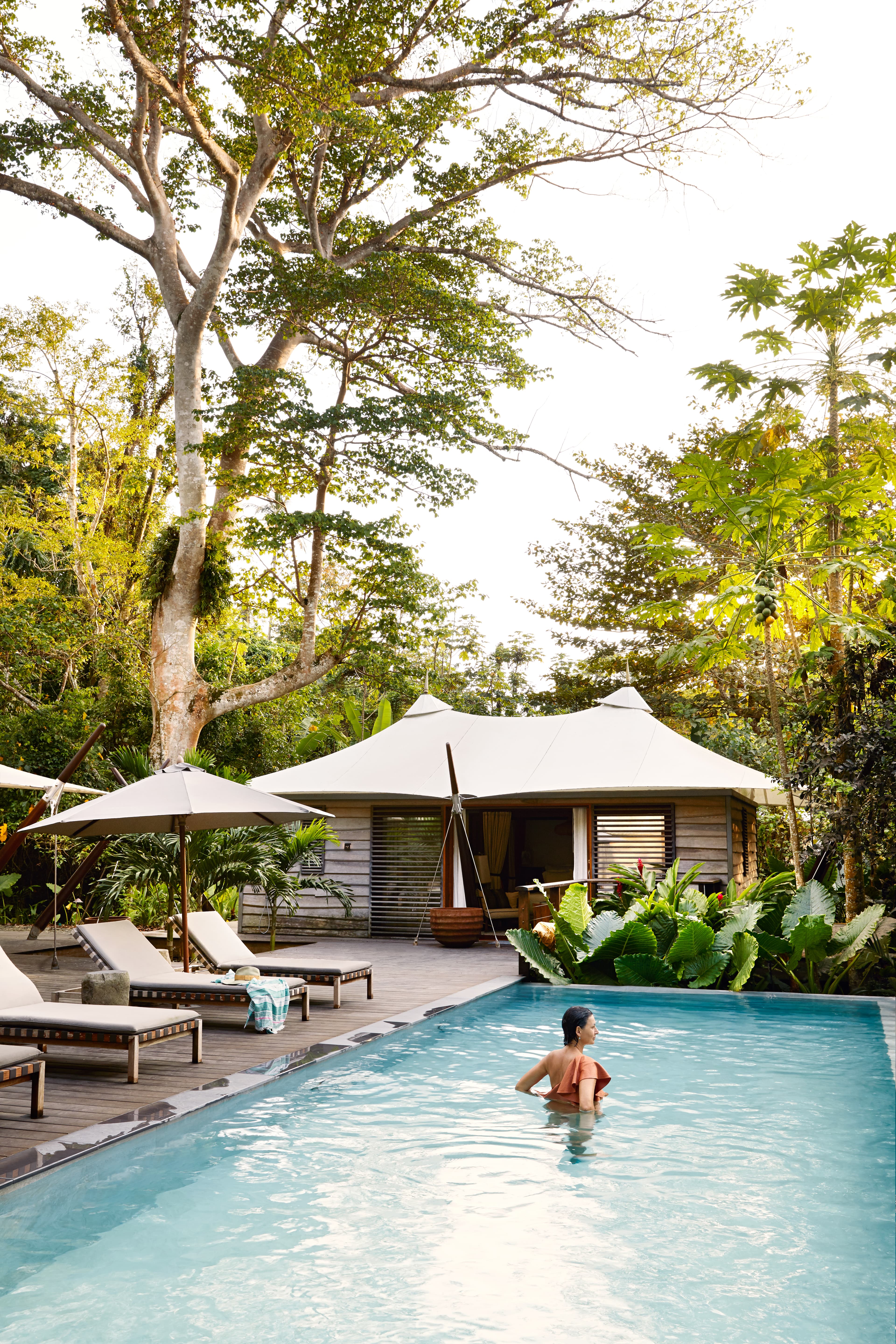 A pool surrounded by greenery, a woman inside, next to it a few sun loungers and a wooden platform at Hotel Sundy Praia