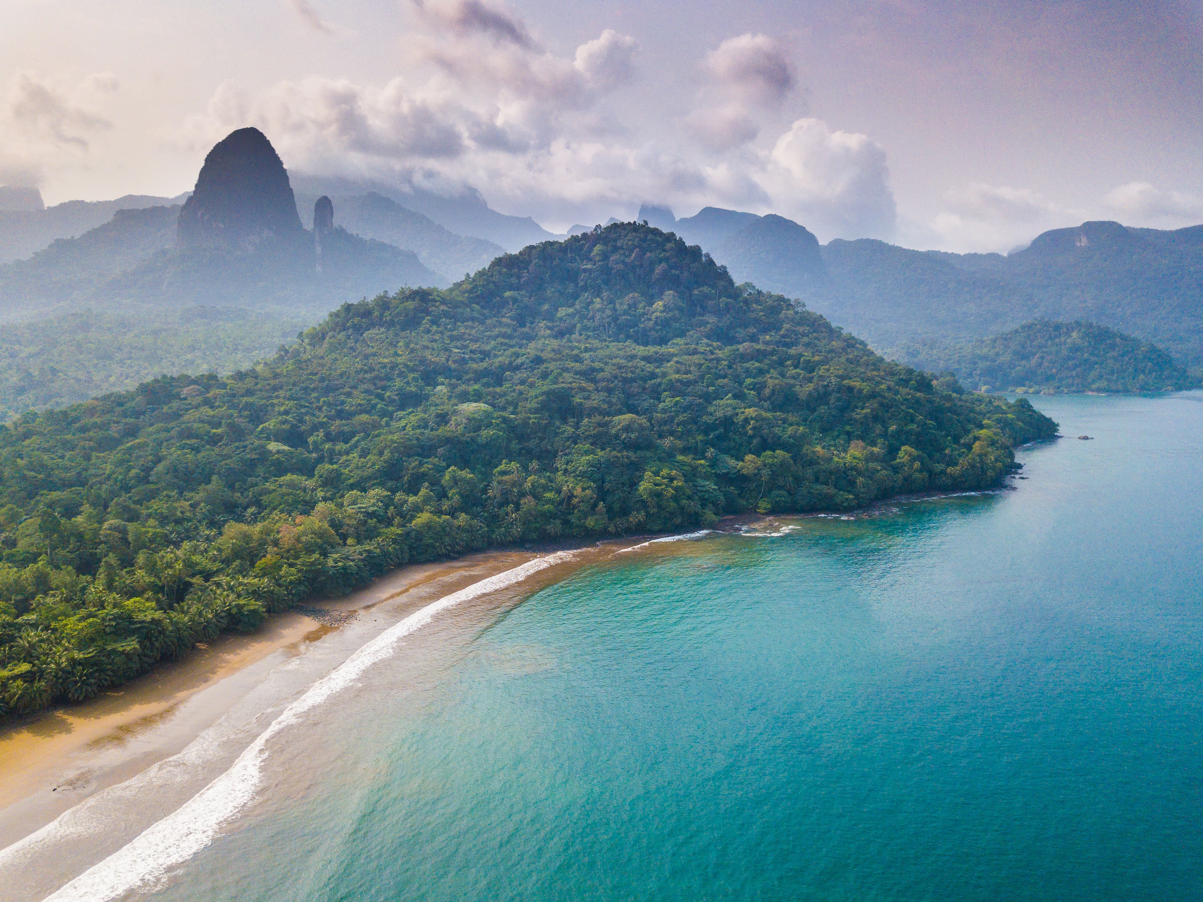 View of Príncipe Island with turquoise water, beach, dense jungle vegetation, and volcanic mountains
